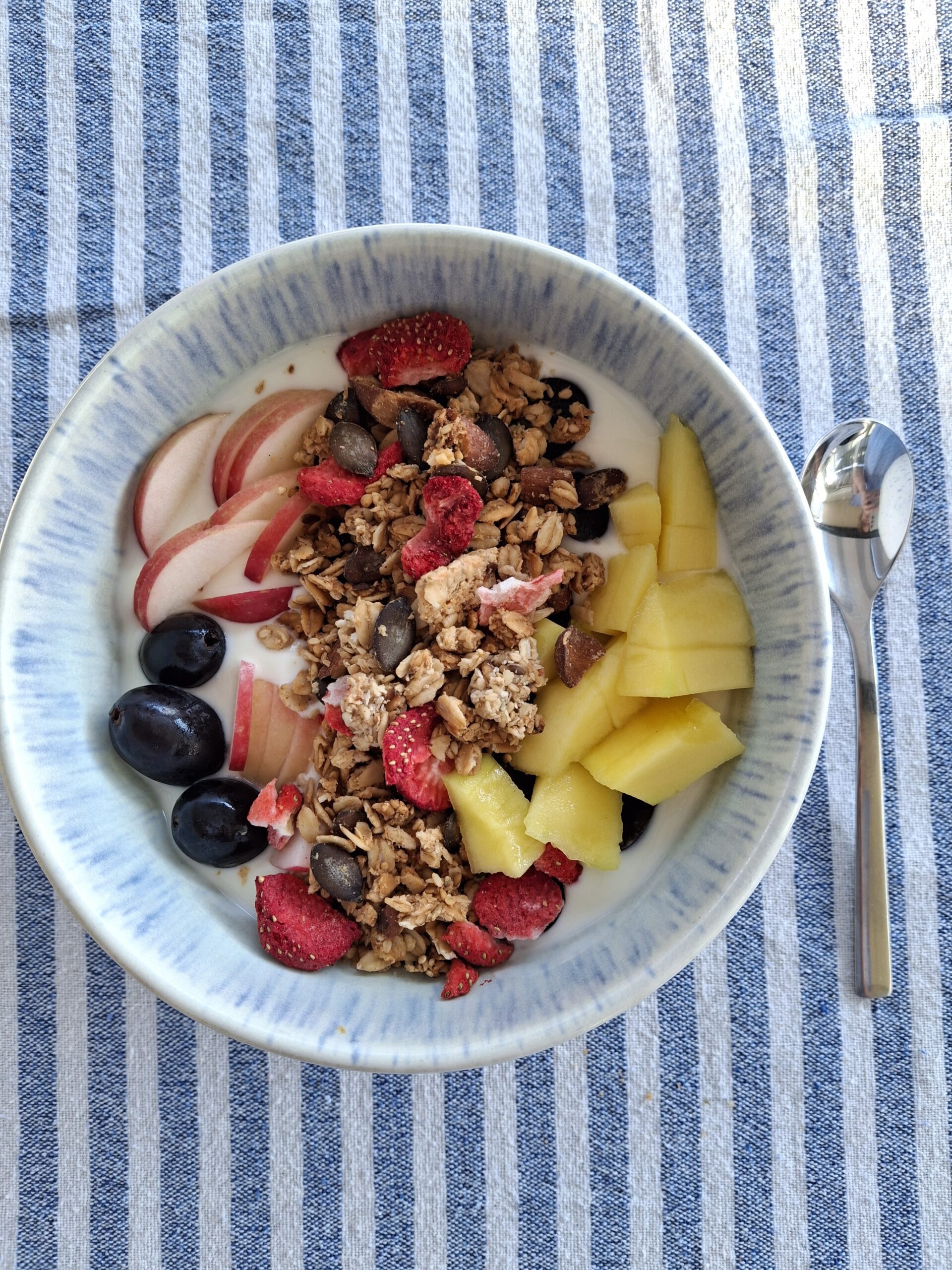 Am bild sieht man ein proteinreiches Granola mit Beeren in einer Schüssel mit Joghurt und Mango und Weintrauben