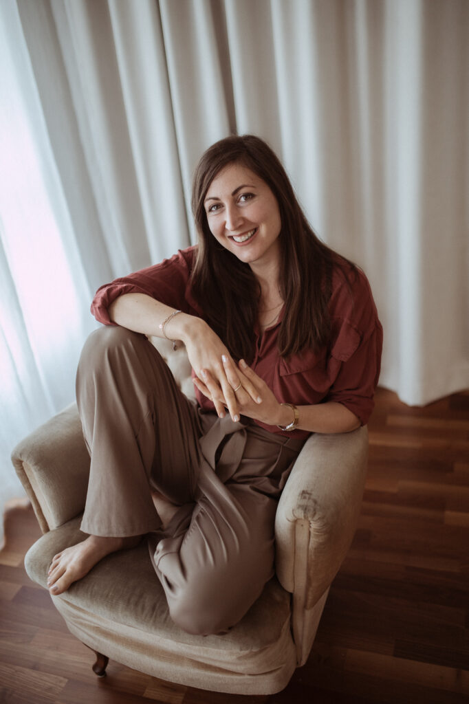 Carina Palm Diätologin sitzt auf einem Stuhl und lächelt in die Kamera